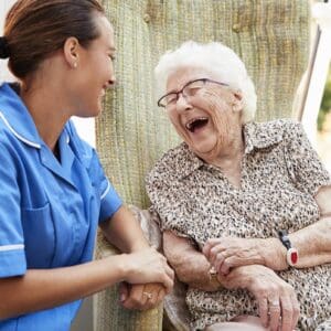 A nurse and elderly woman sharing a joyful moment outdoors.