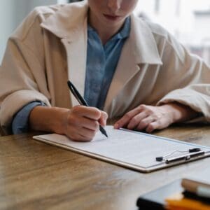 Person writing on a clipboard at a wooden table.