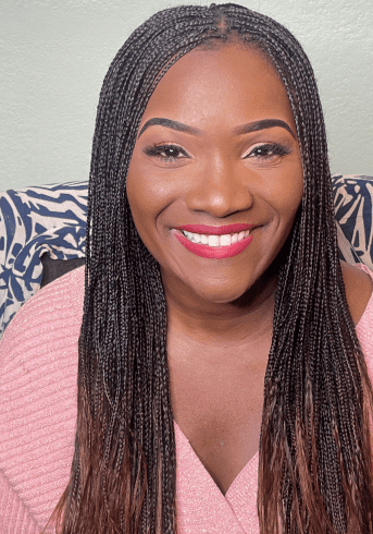 Smiling woman with long braided hair wearing a pink top.