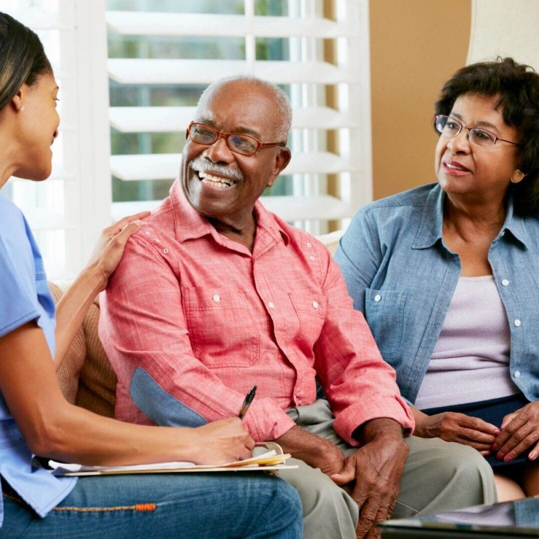 A healthcare professional consulting with an elderly couple in a bright room.